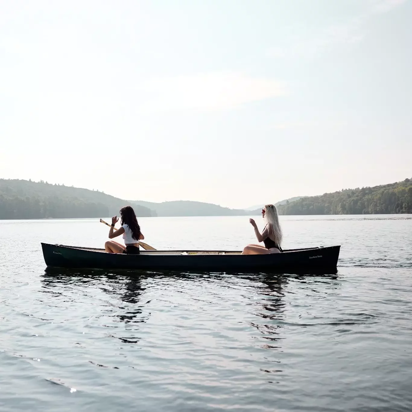 Two women sharing a canoe on a calm lake surrounded by forest.